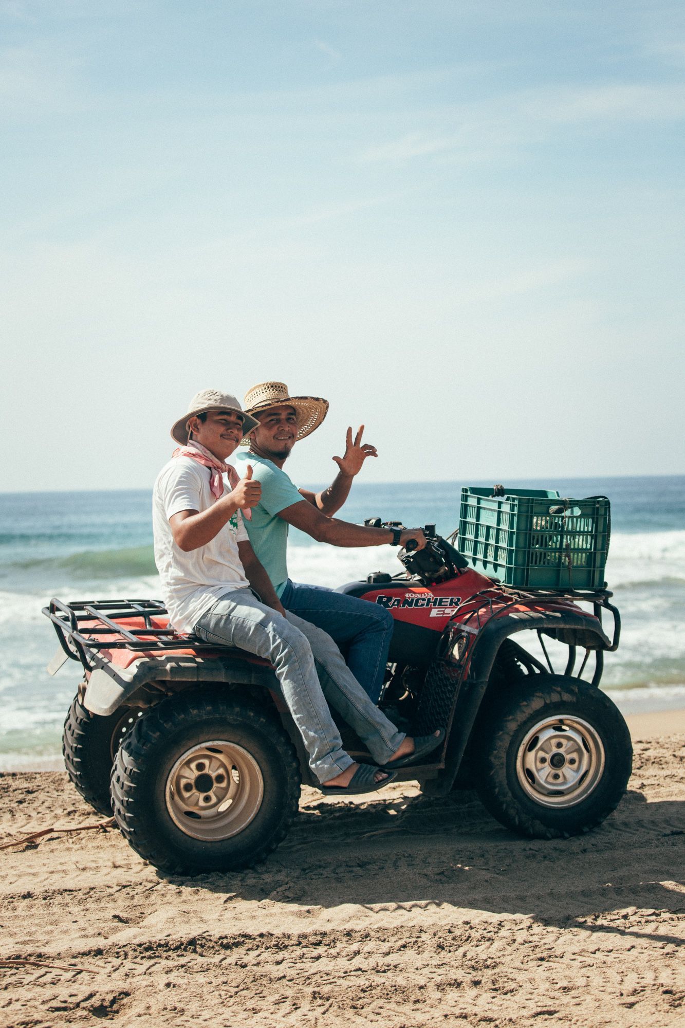 Two men are riding an atv on the beach.