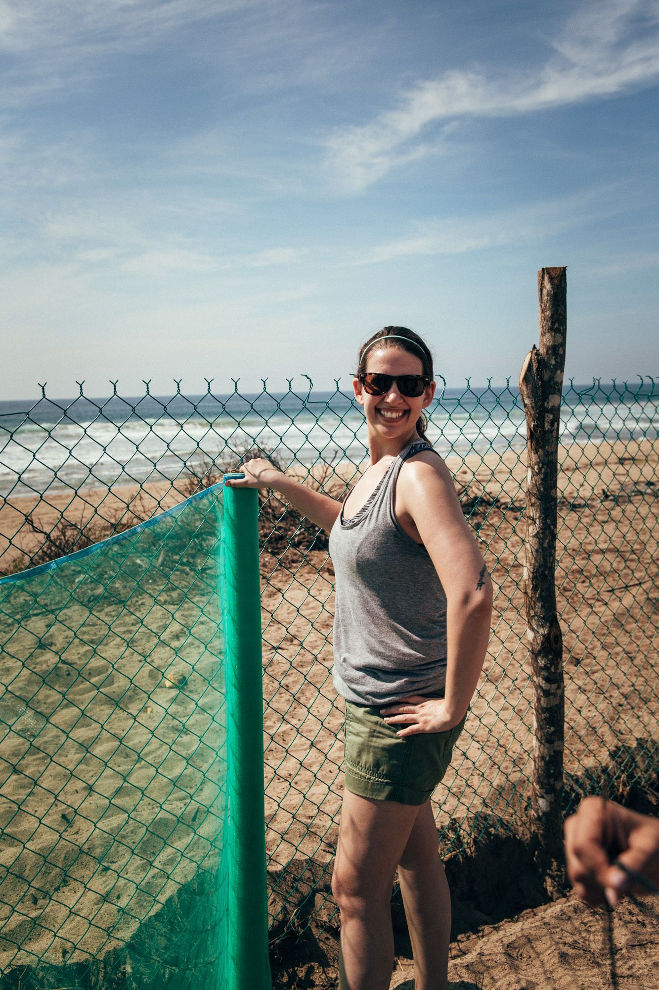 A woman is standing next to a chain link fence on the beach.