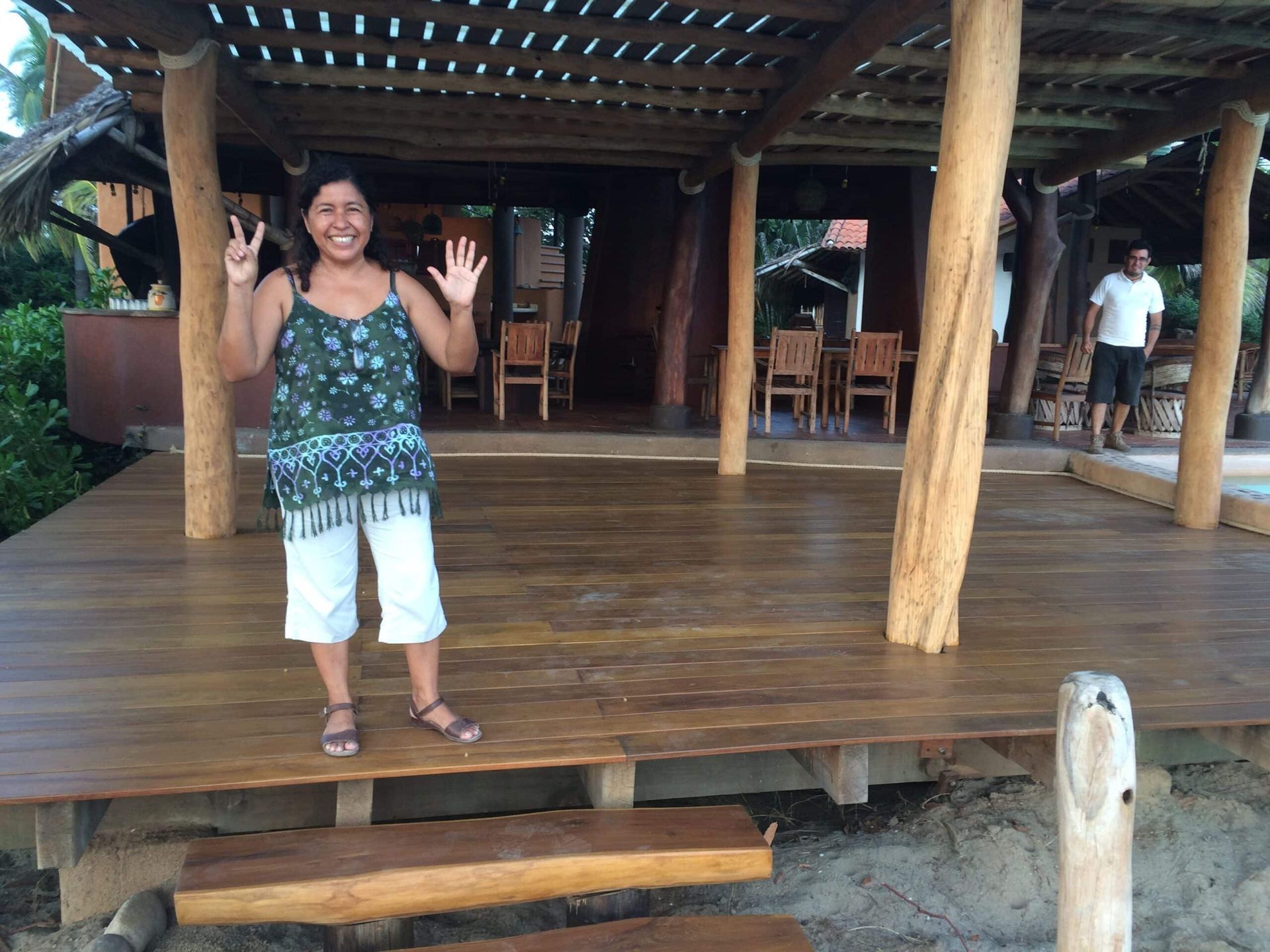 A woman standing on a wooden deck giving a peace sign
