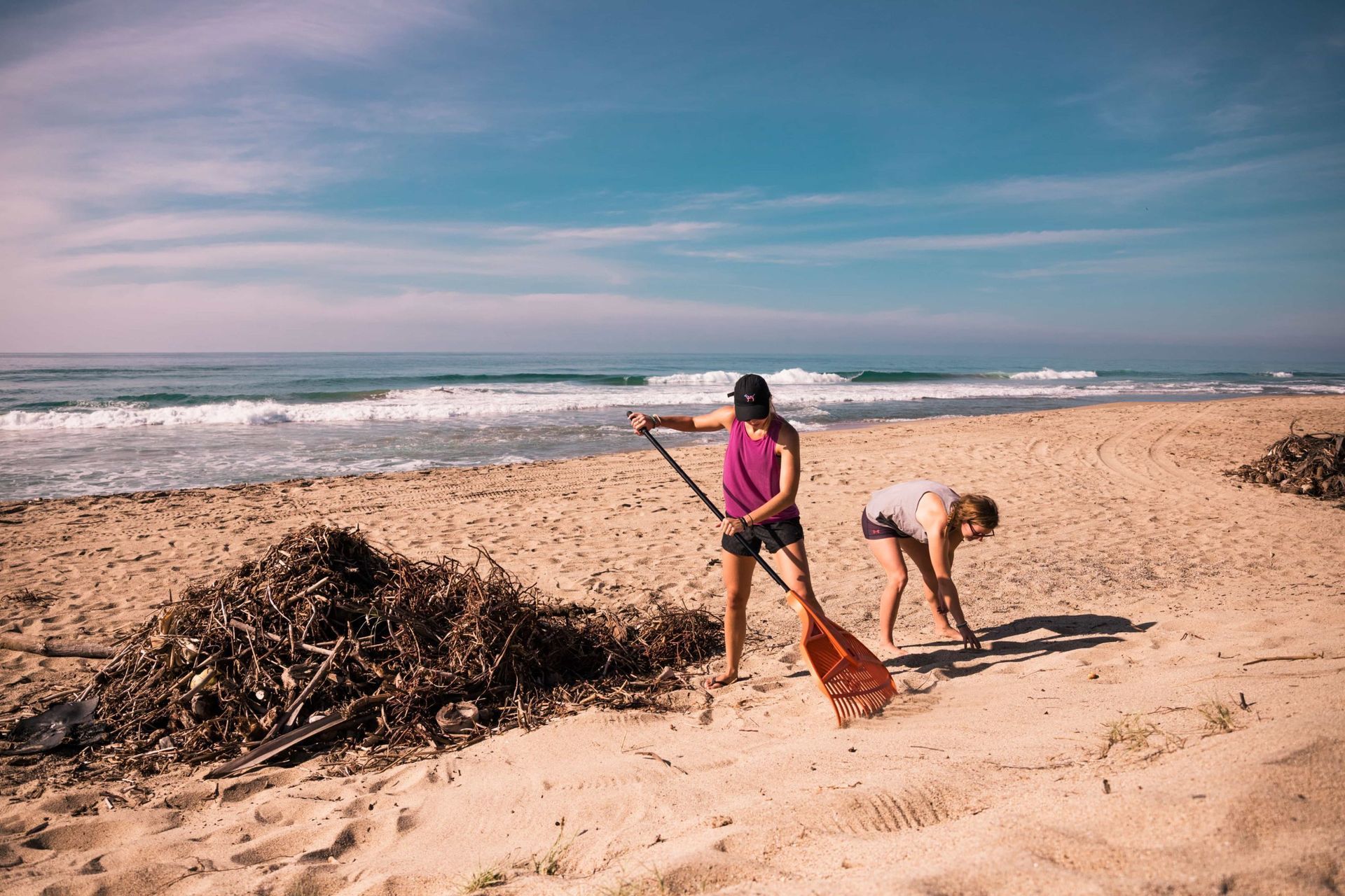 Two people are raking the sand on a beach.