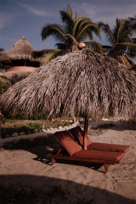 Two lounge chairs under an umbrella on a beach