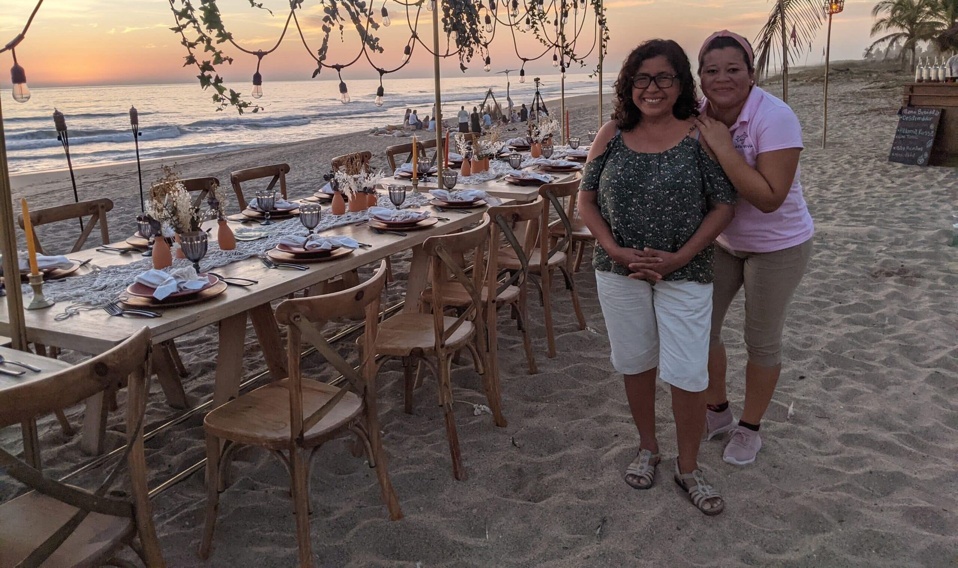Two women are standing next to a long table on the beach.