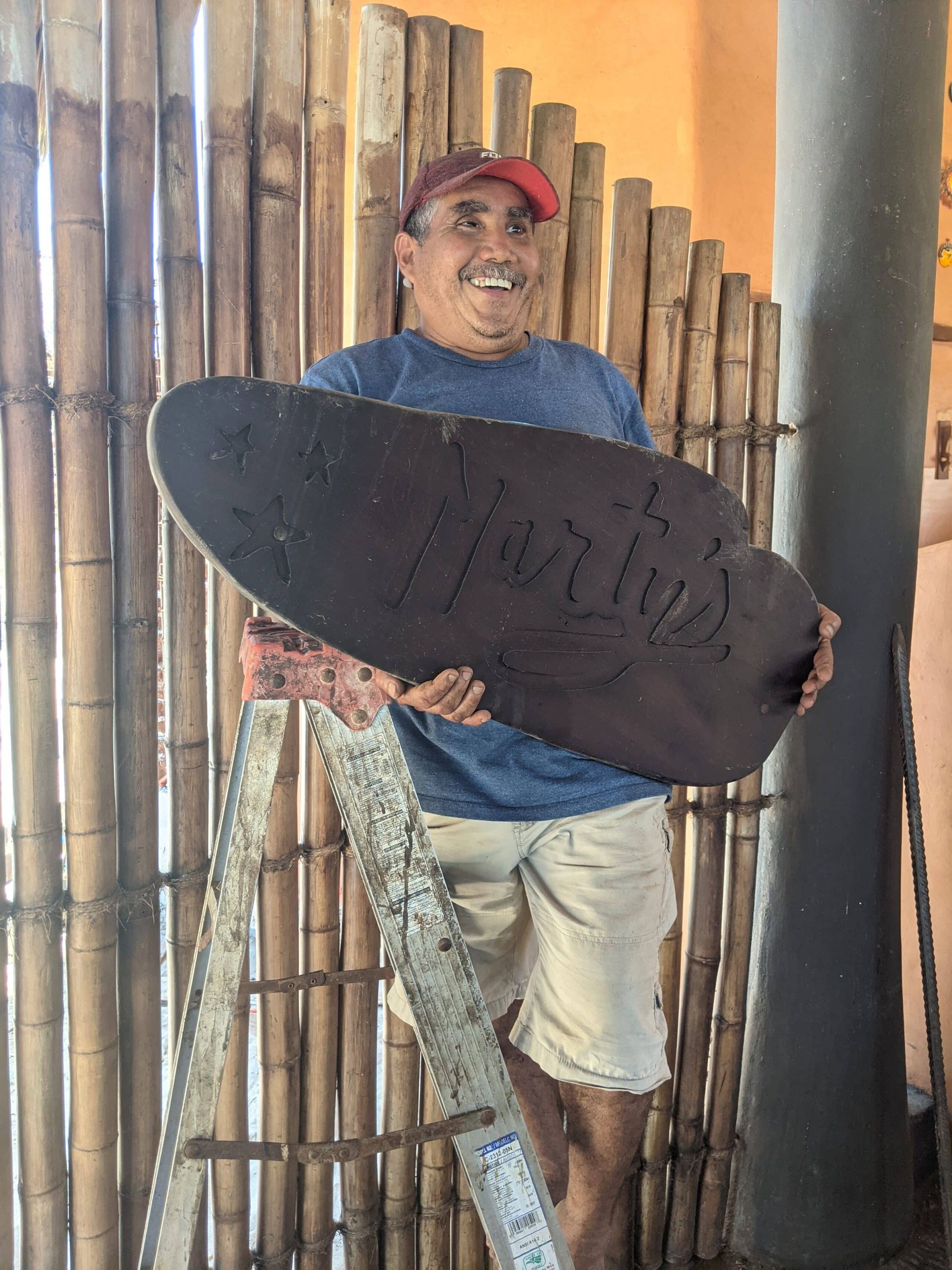 A man standing on a ladder holding a surfboard that says ' surfing ' on it
