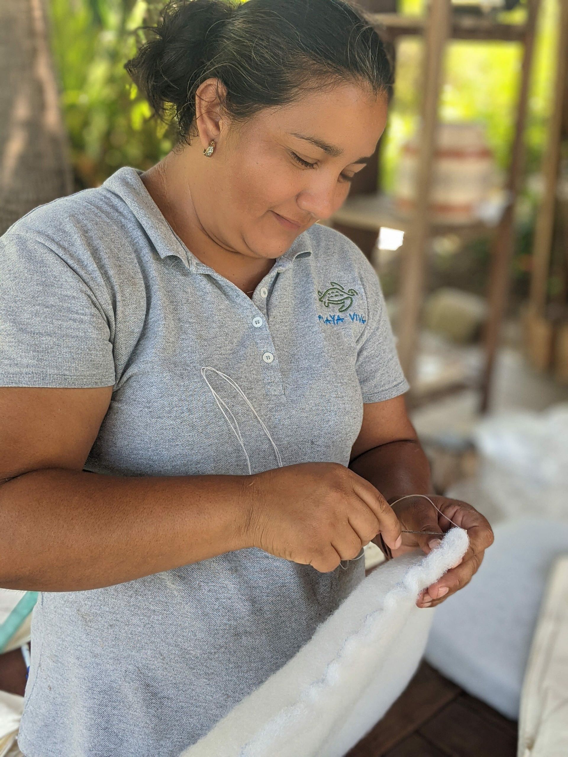 A woman in a gray shirt is working on a piece of fabric.