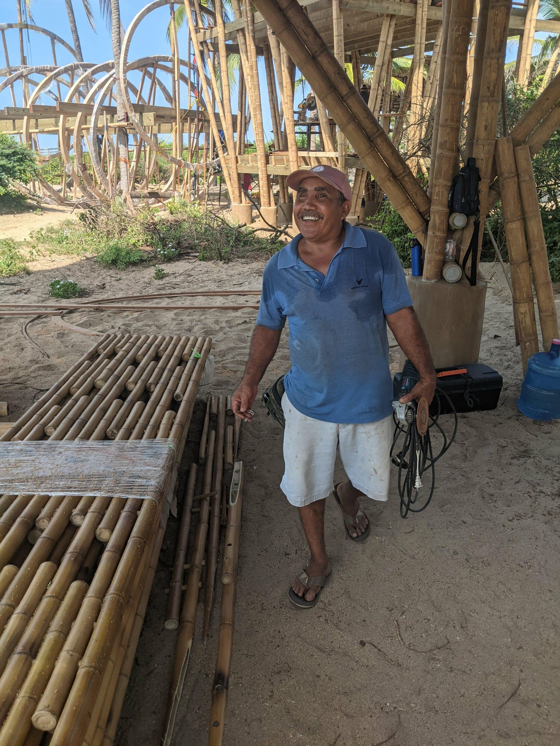 A man in a blue shirt and white shorts is standing in front of a pile of bamboo poles.