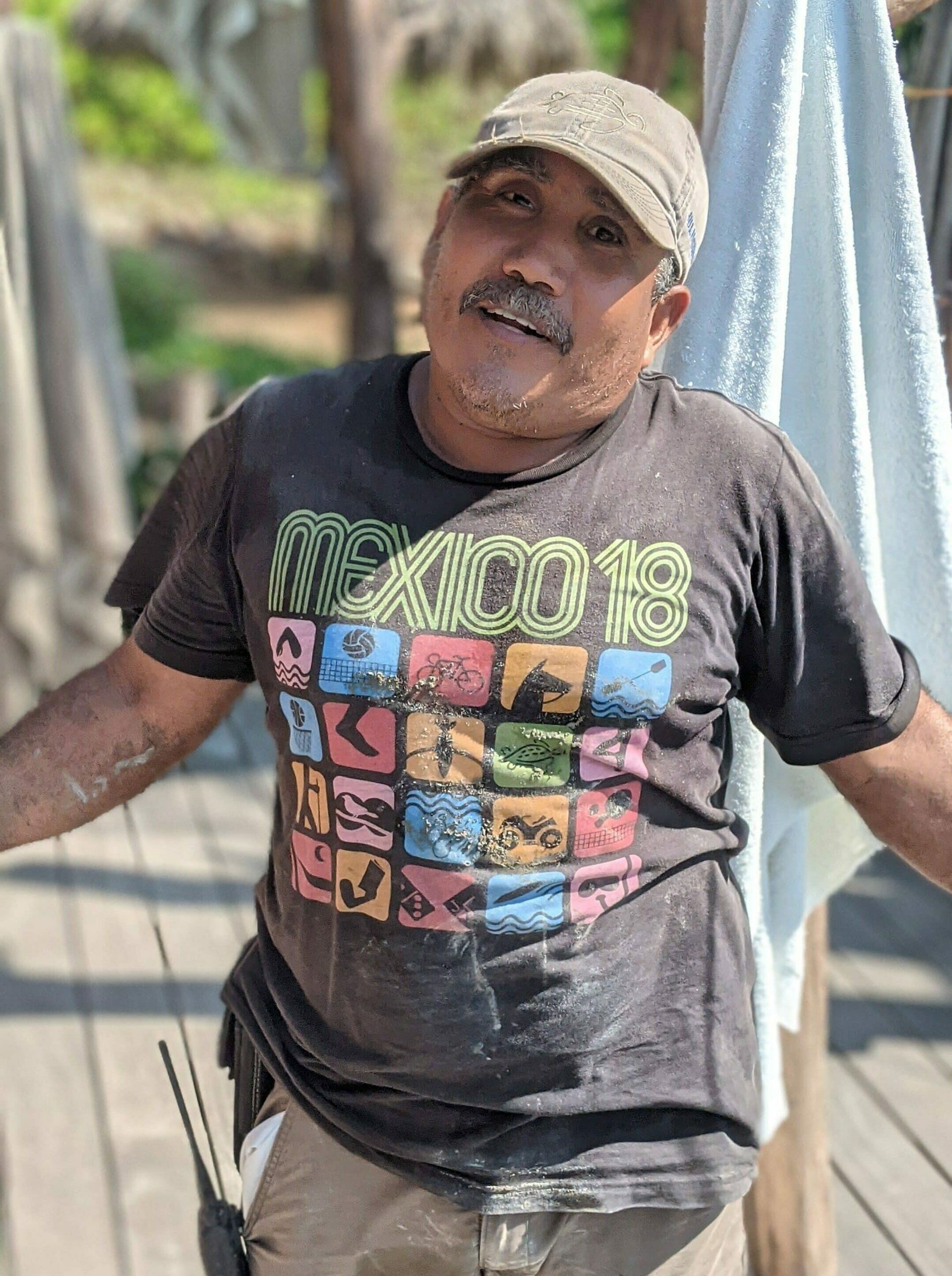 A man wearing a t-shirt that says mexico is standing on a wooden deck.