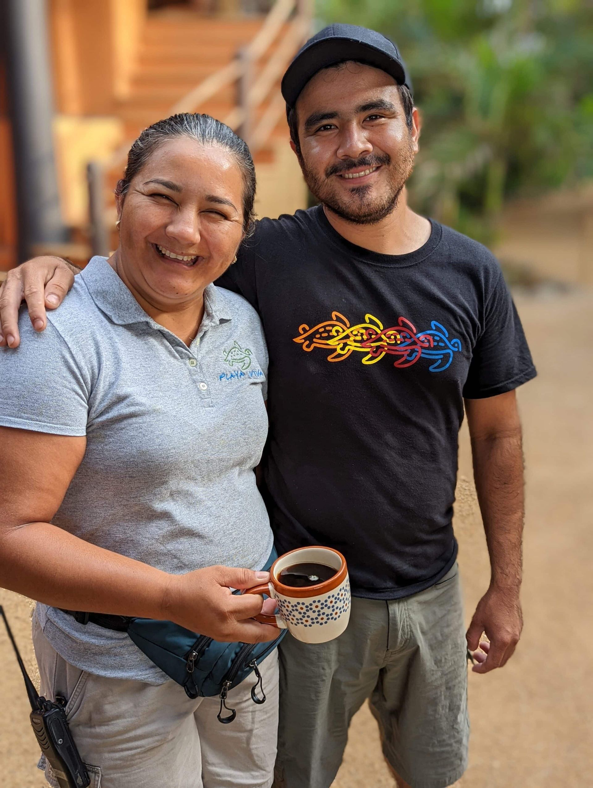 A man and a woman are posing for a picture while the woman is holding a cup of coffee.