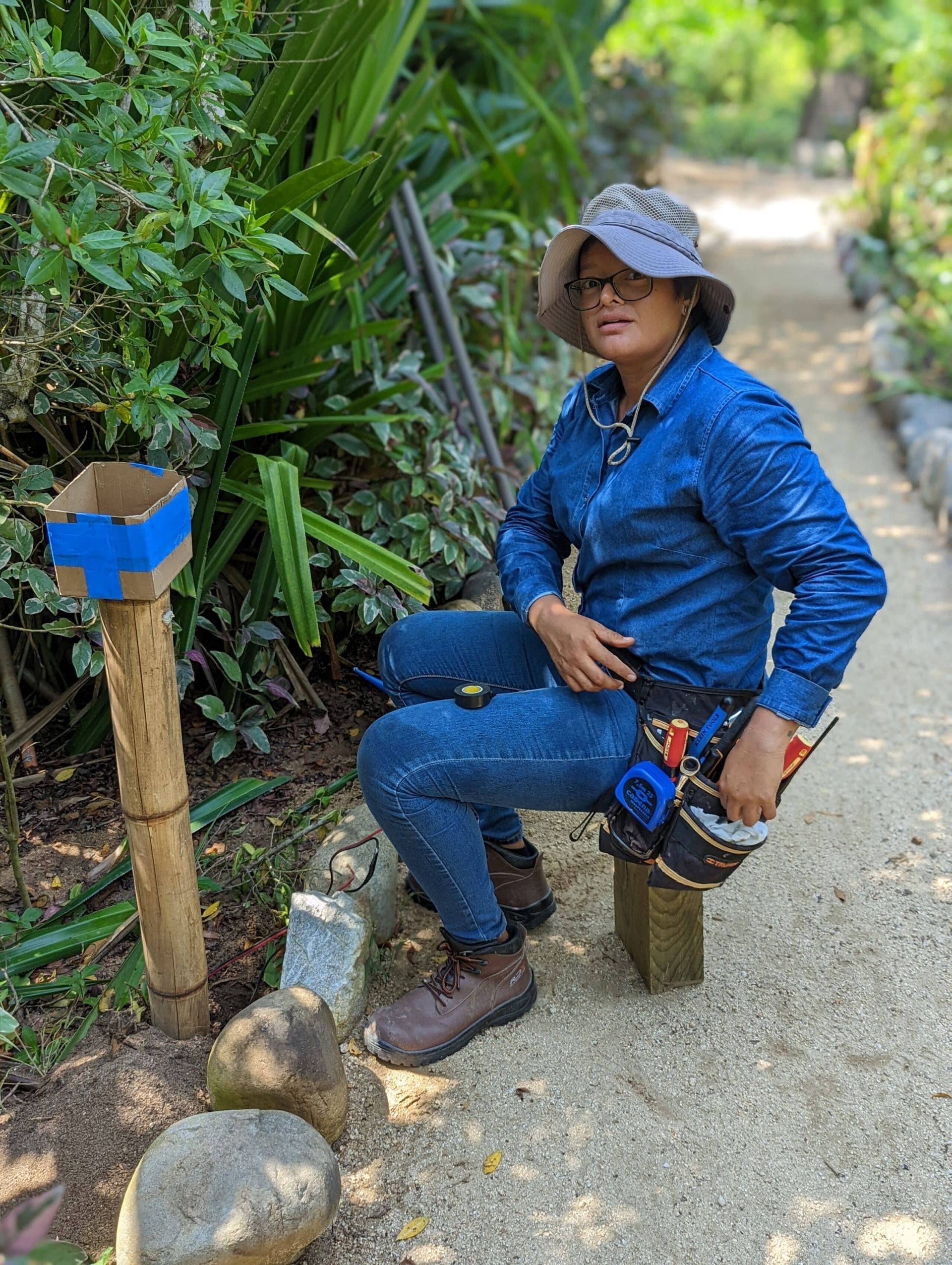A woman is sitting on a wooden bench in a garden.