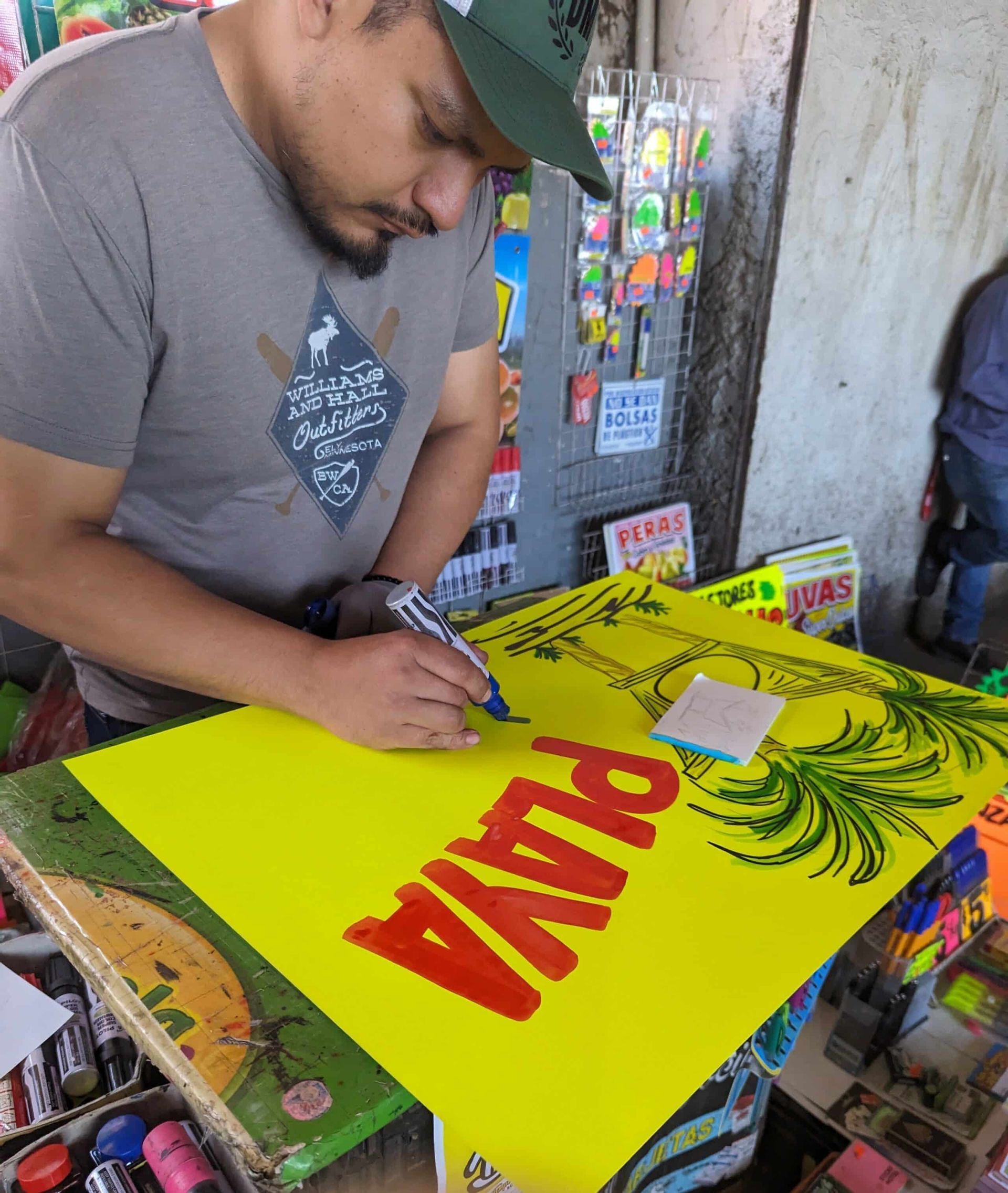 A man is writing on a yellow sign that says pita