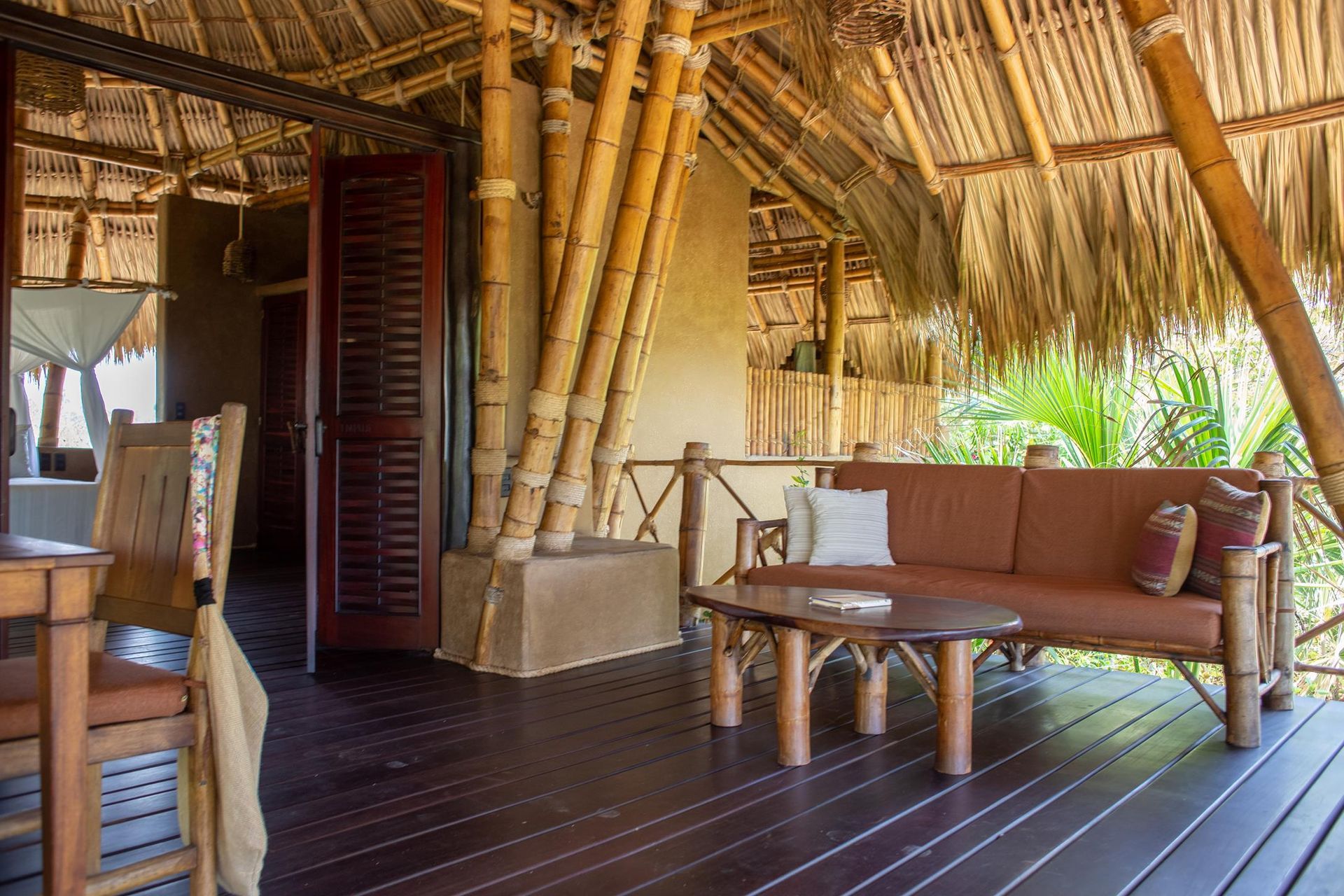 A living room with a couch , table and chairs under a thatched roof.