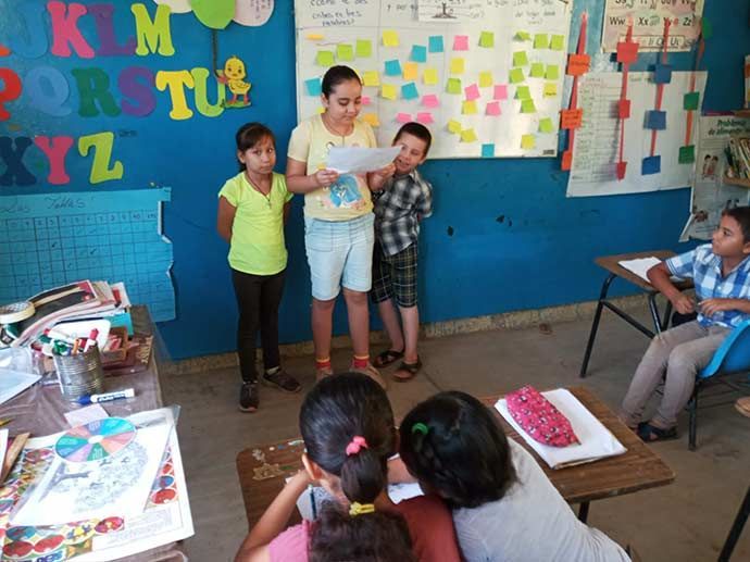 A group of children are standing in front of a wall that has the alphabet on it