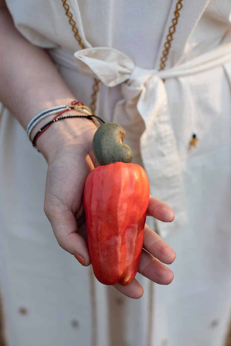 A woman in a white dress is holding a red pepper in her hand.