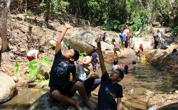 Two young boys are sitting on a rock near a river.