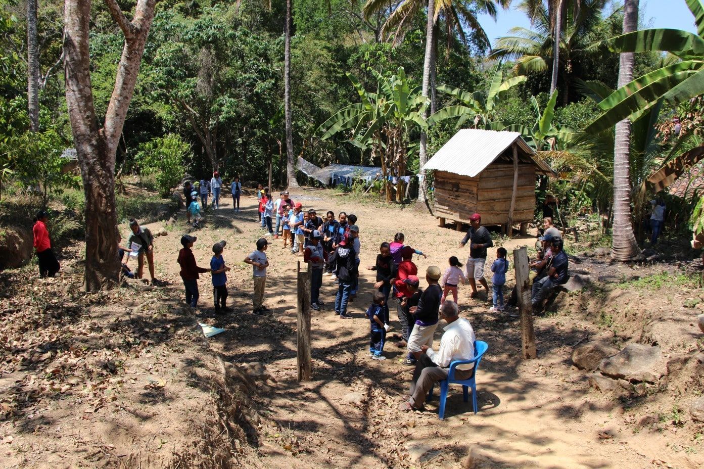 A group of people are standing around a small hut in the middle of a forest.