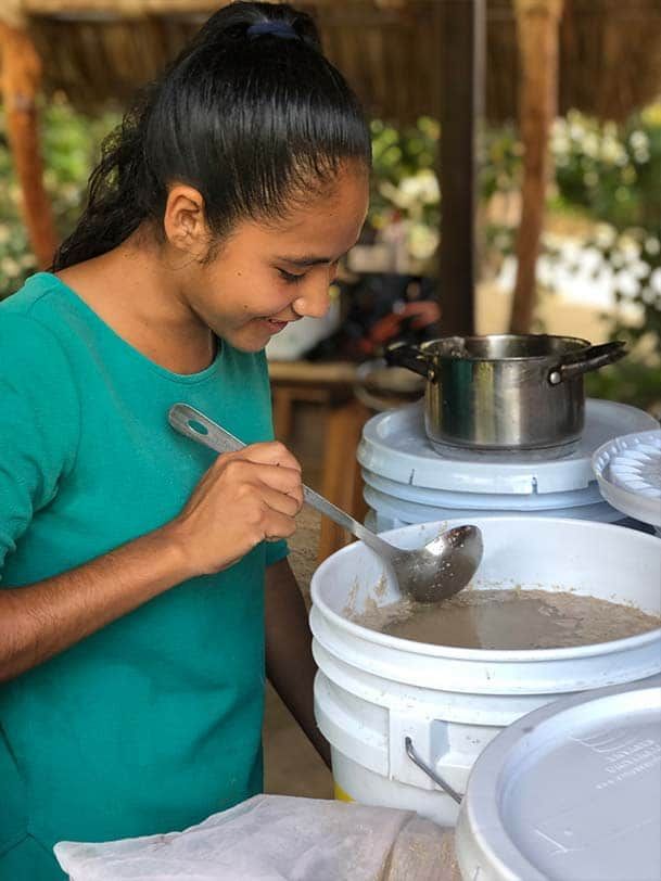 A woman is scooping something out of a bucket with a ladle.