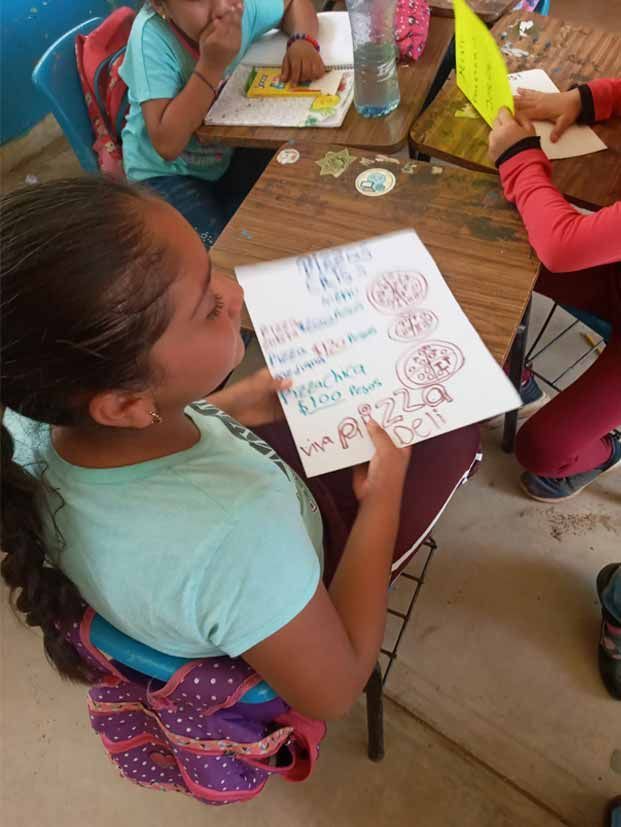 A girl is sitting at a desk with a piece of paper in her hand.