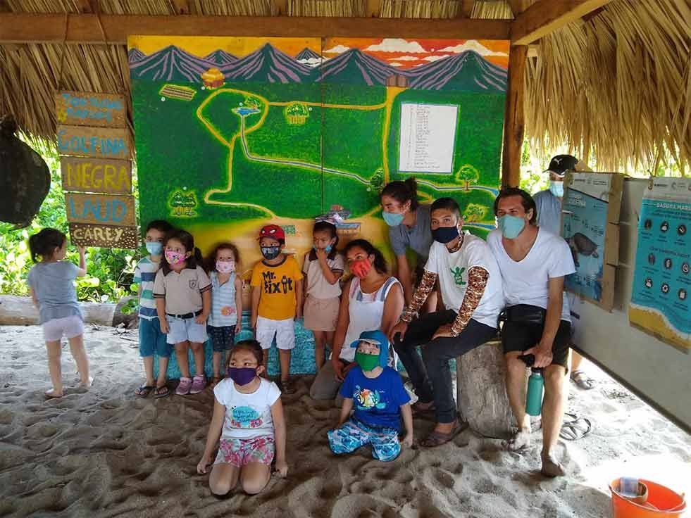 A group of people wearing masks are posing for a picture in front of a mural.