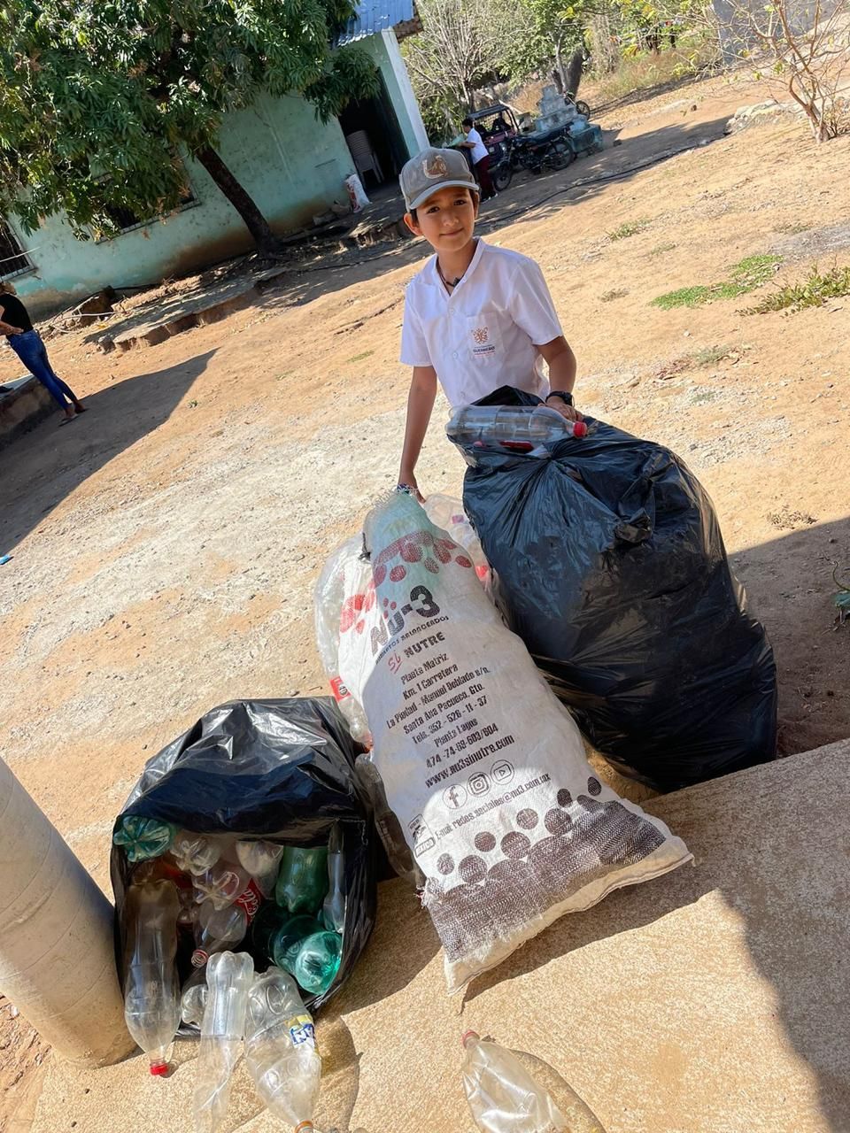 A boy is standing next to a large bag of trash.