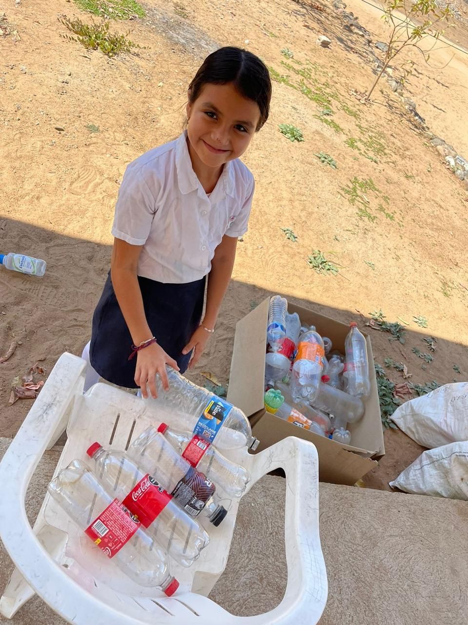 A young girl is standing next to a table full of empty coca cola bottles