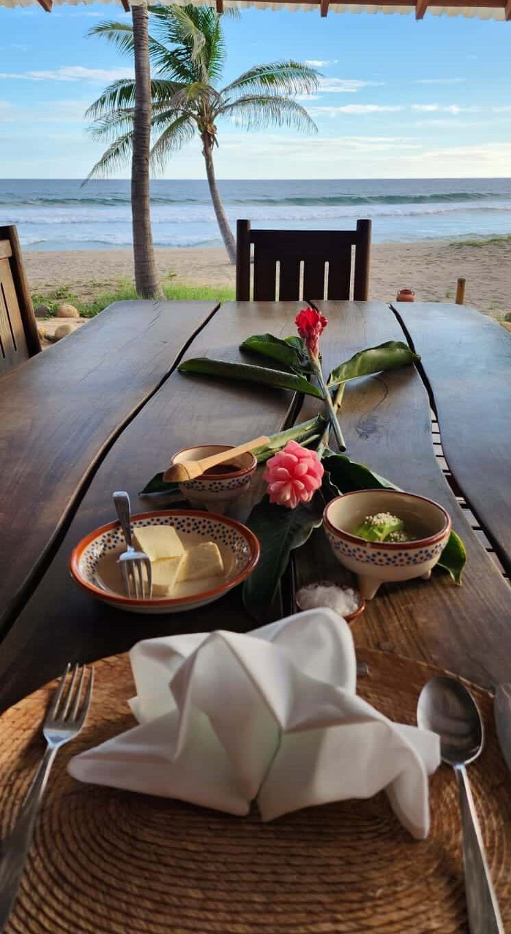 A table with plates of food and utensils on it with a view of the ocean.