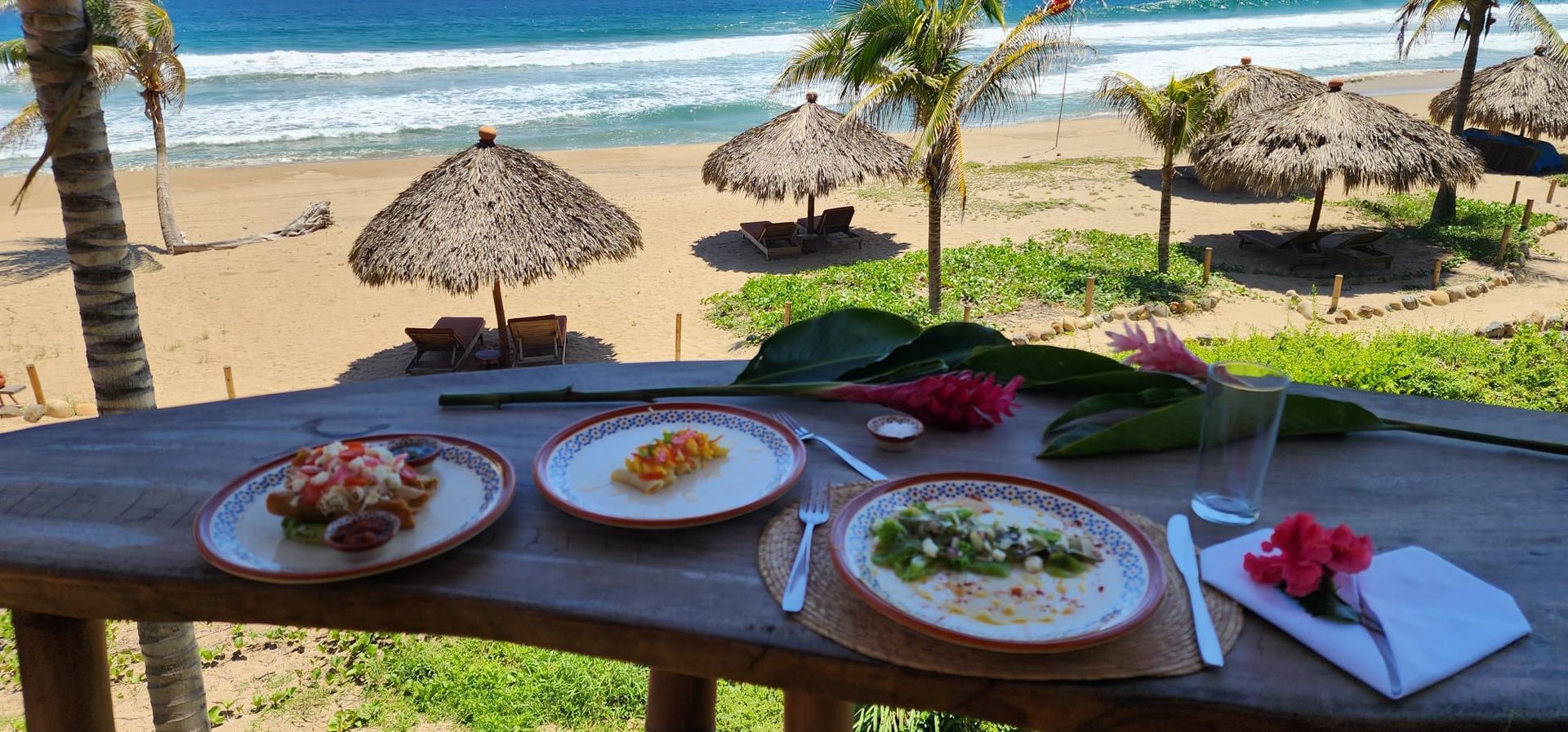 A wooden table topped with three plates of food and umbrellas on a beach.