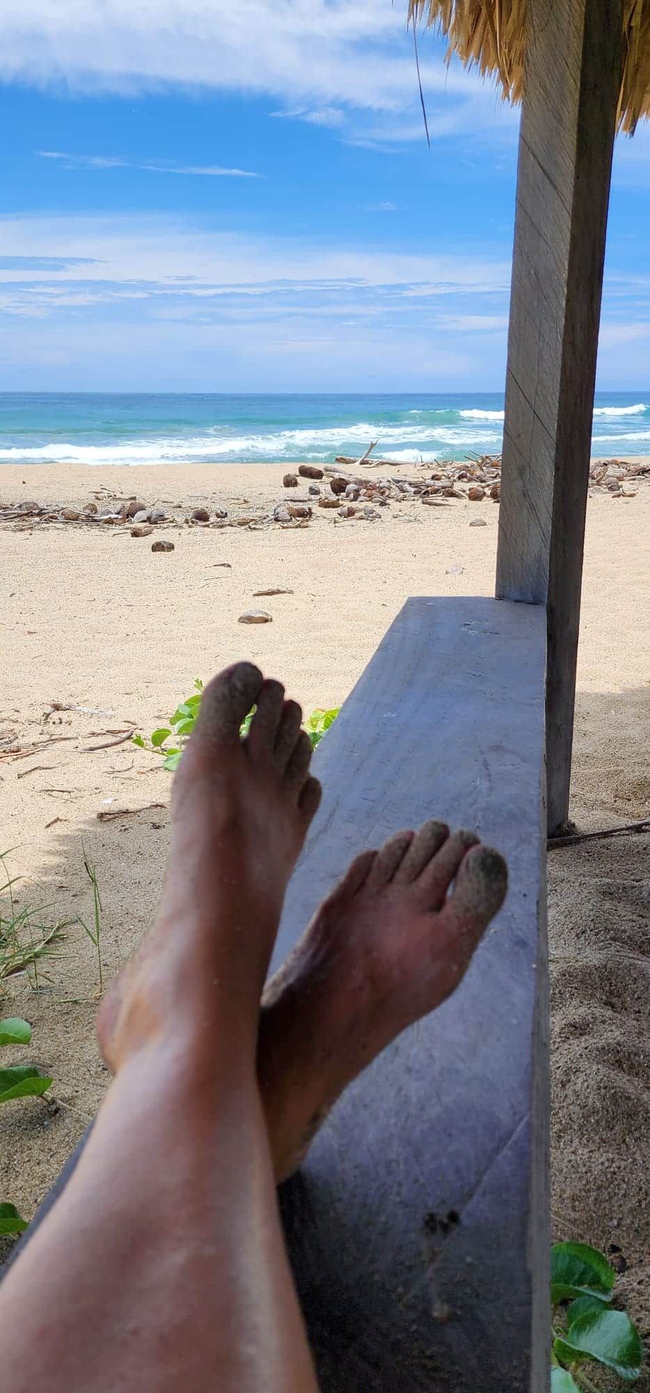 A person is sitting on a bench with their feet up on the beach.