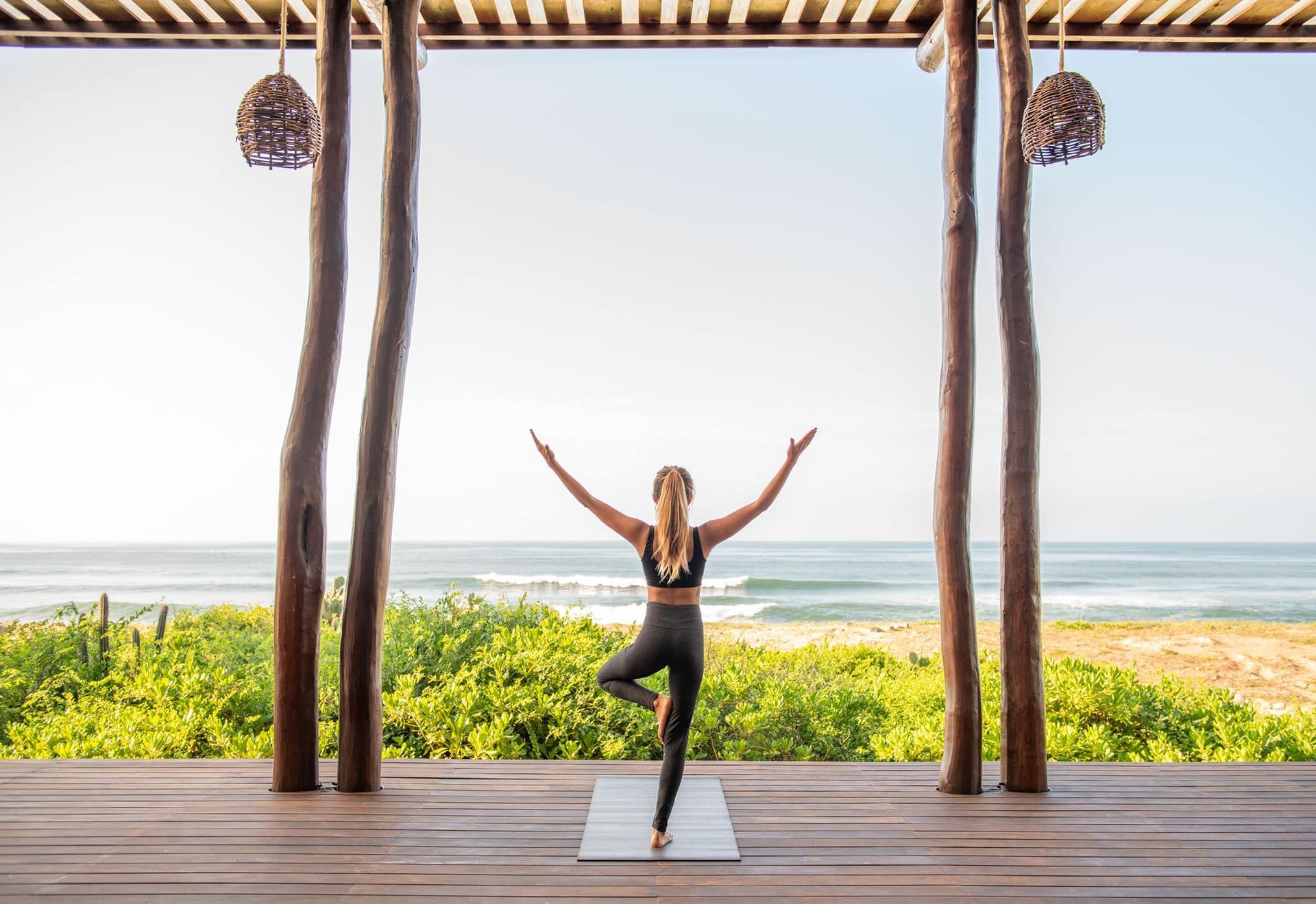 A woman is practicing yoga on a wooden deck overlooking the ocean.