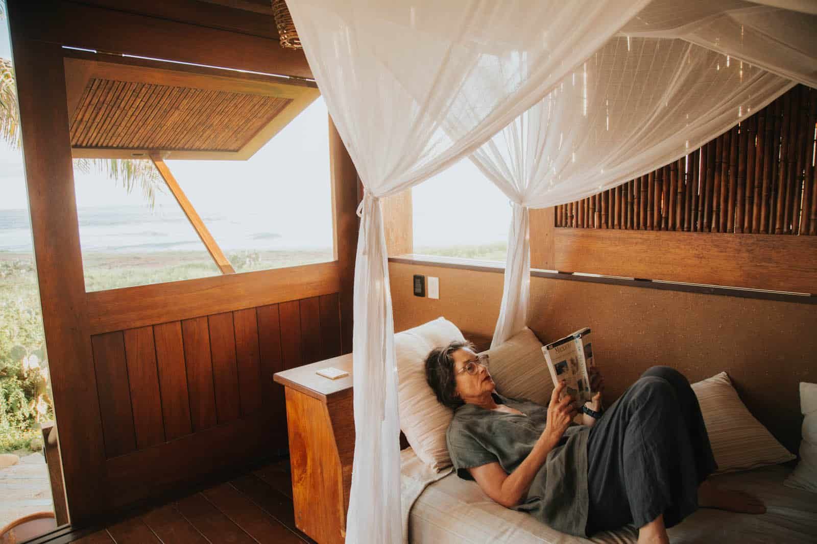 A woman is laying on a canopy bed reading a book.