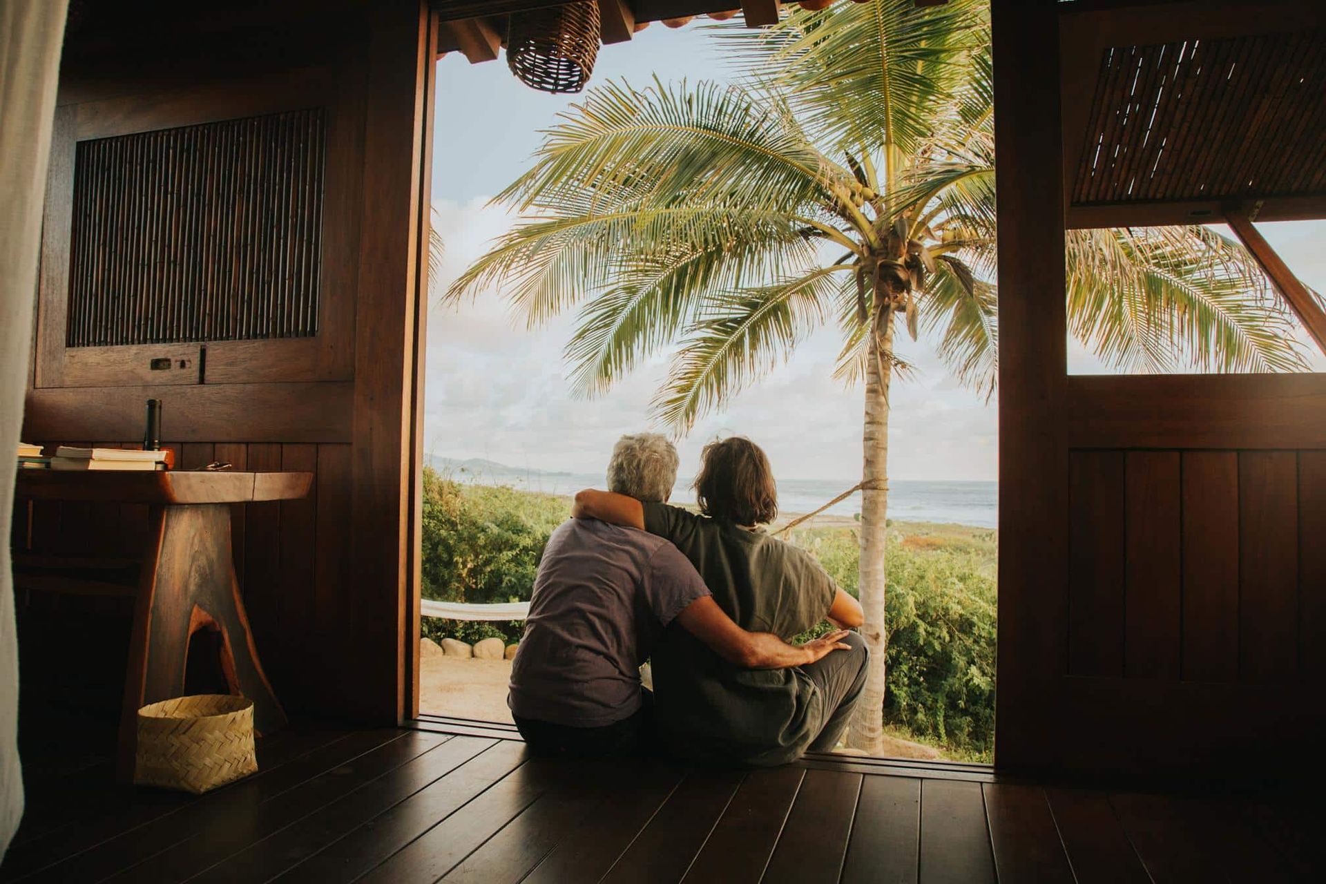 A man and a woman are sitting on the floor looking out of a window at the ocean.