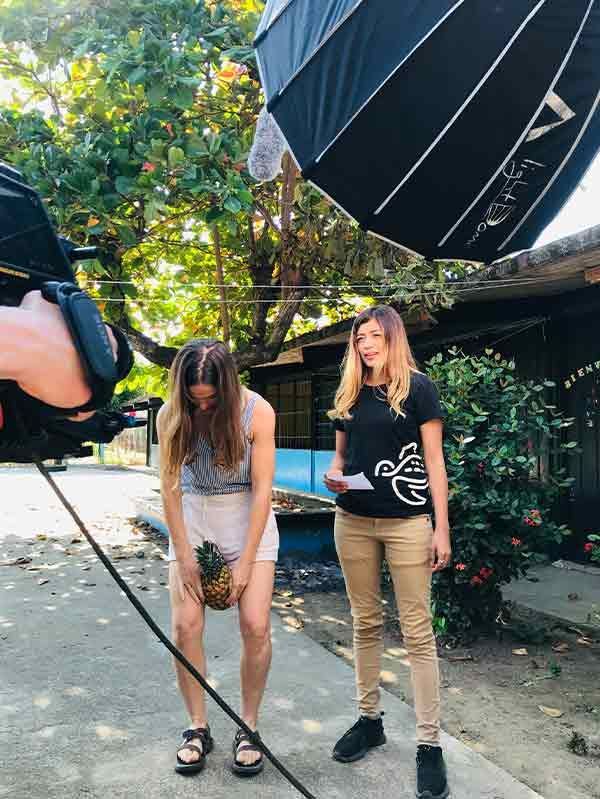 Two women are standing next to each other on a sidewalk holding pineapples.
