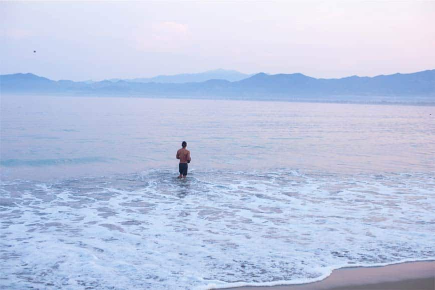 A man is standing in the ocean on a beach.