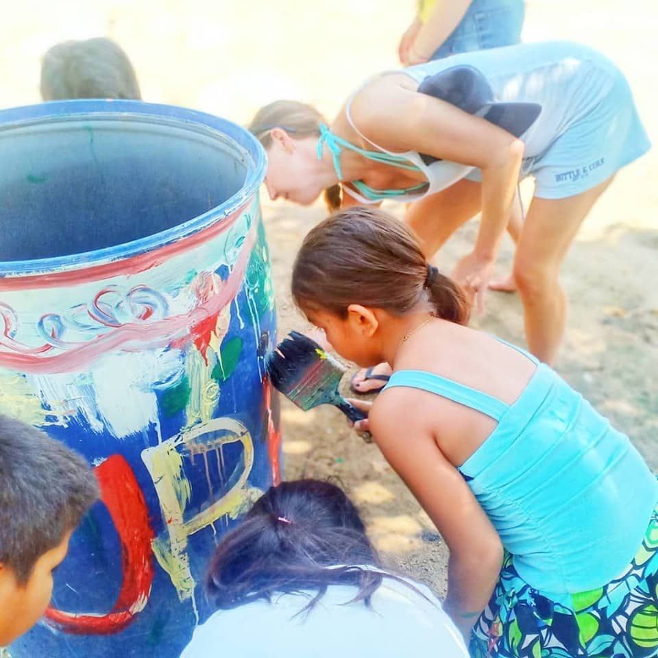 A group of children are painting a barrel with the letter p on it
