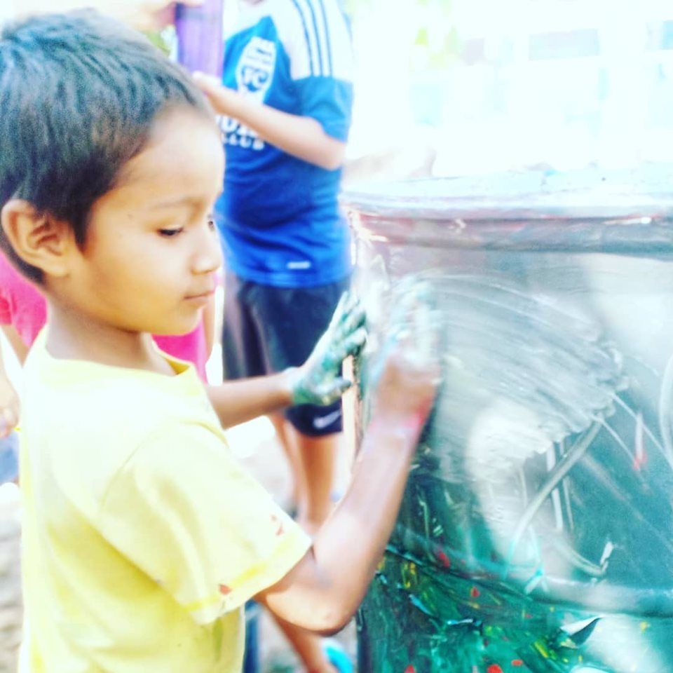A young boy in a yellow shirt is playing with a bucket of paint