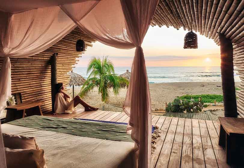 A woman is sitting on a bed in a room with a view of the ocean.