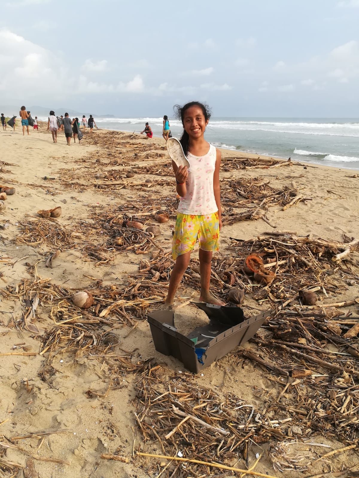 A young girl is standing on a beach holding a bottle.