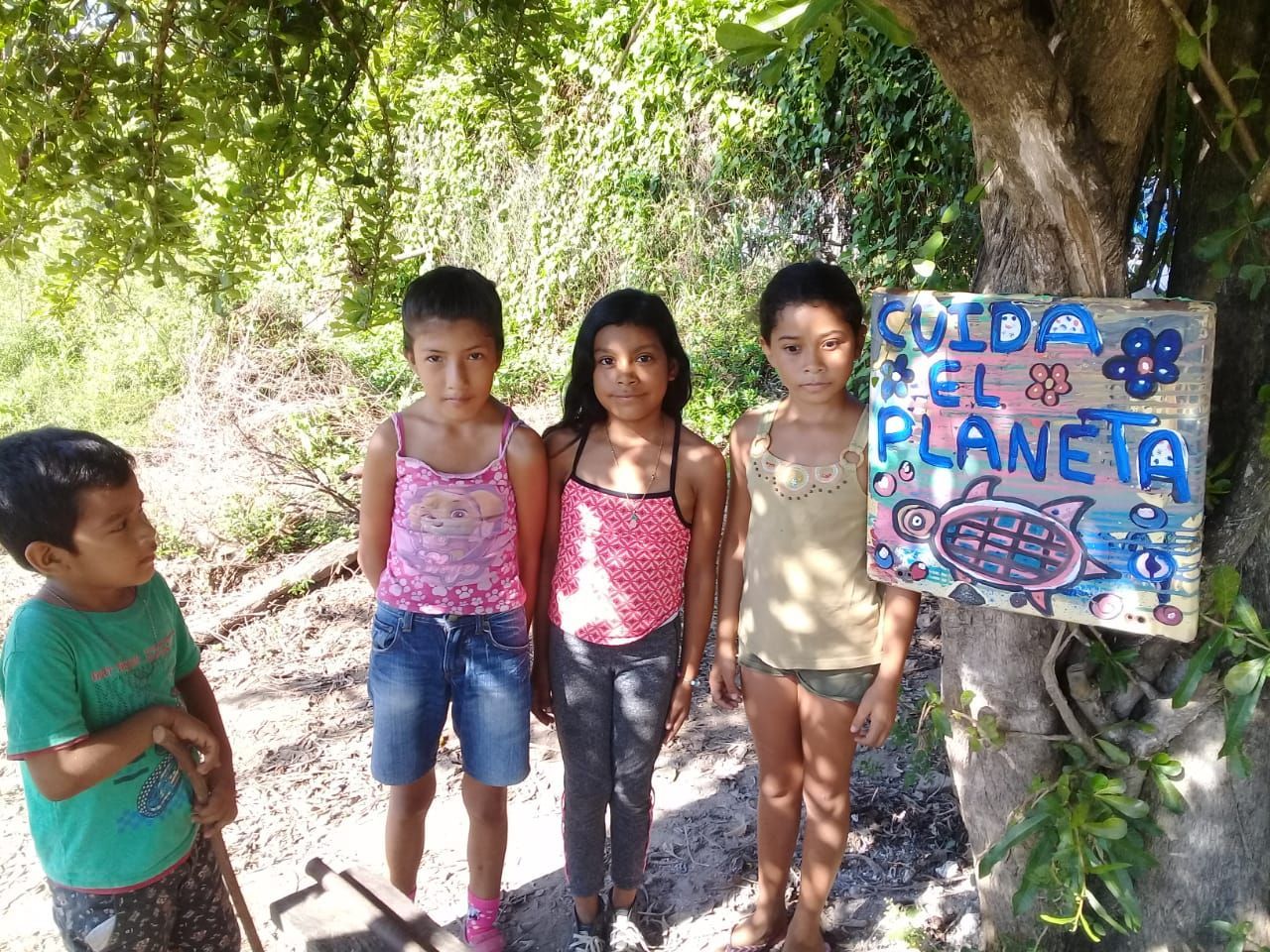 A group of children standing in front of a tree with a sign that says ' suelta el planeta ' on it