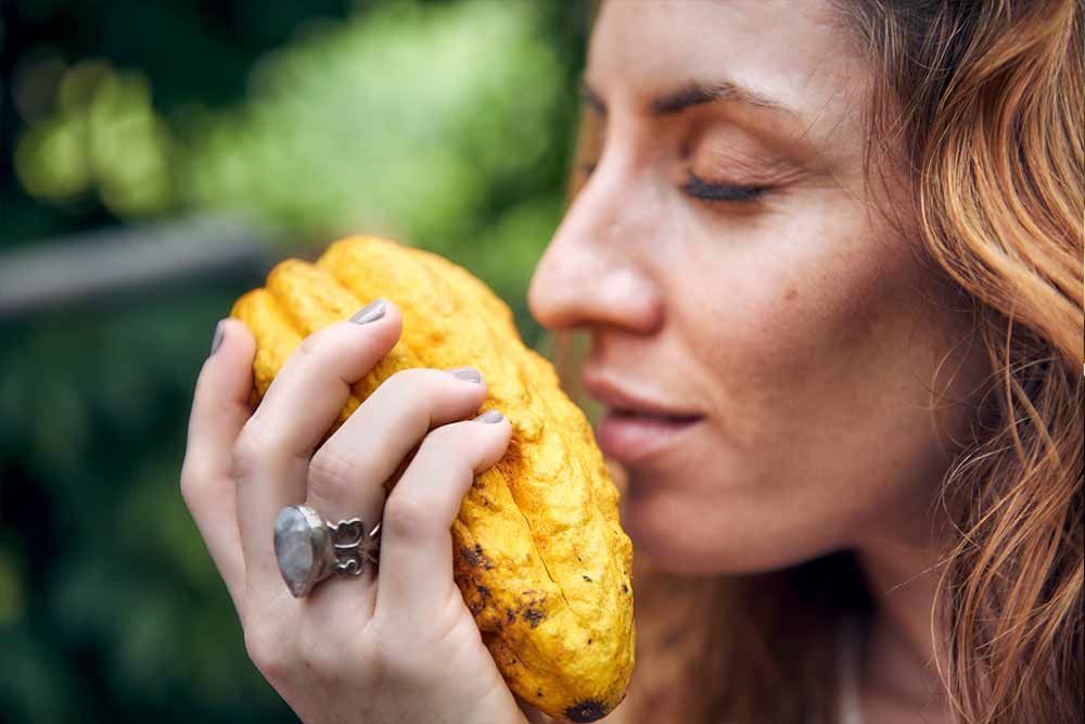 A woman with a ring on her finger is smelling a yellow fruit.