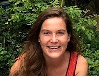 A woman is smiling for the camera in front of a bush.