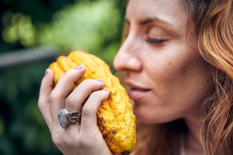A woman with a ring on her finger is smelling a yellow fruit.