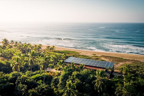 An aerial view of a beach with palm trees and a building with solar panels on it.