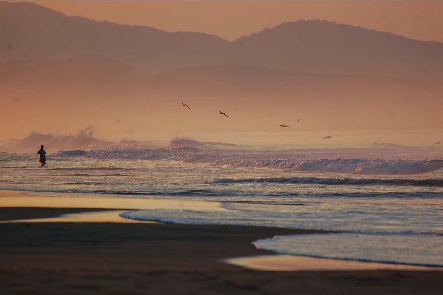 A person is walking on the beach at sunset.