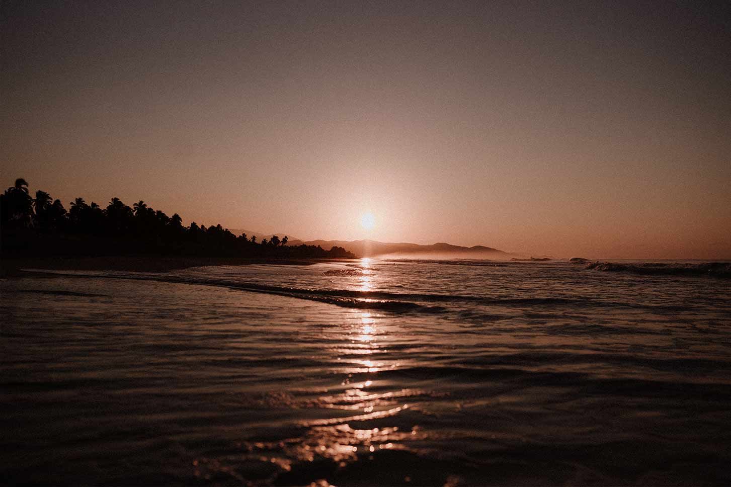 The sun is setting over the ocean on a beach.