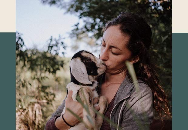 A woman is holding a baby goat in her arms and kissing it.