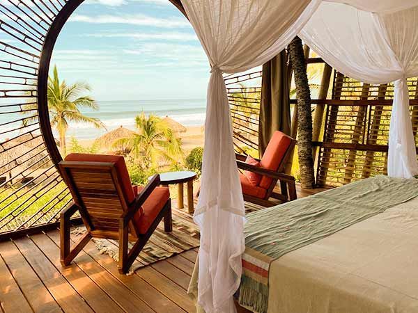 A bedroom with a canopy bed and chairs with a view of the ocean