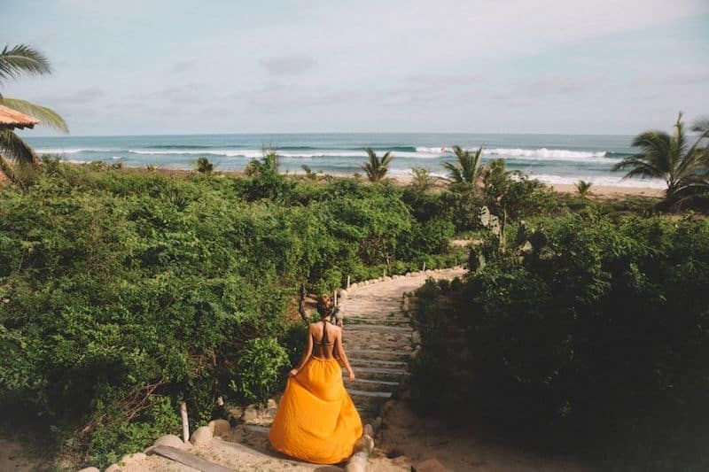 A woman in a yellow dress is walking down stairs to the beach.
