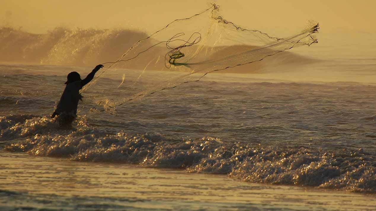 A man is flying a kite in the ocean at sunset.