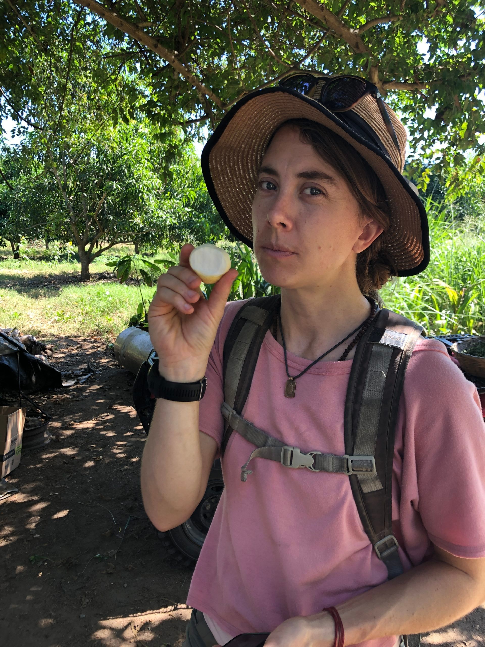 A woman wearing a hat and a pink shirt is holding an egg in her hand.