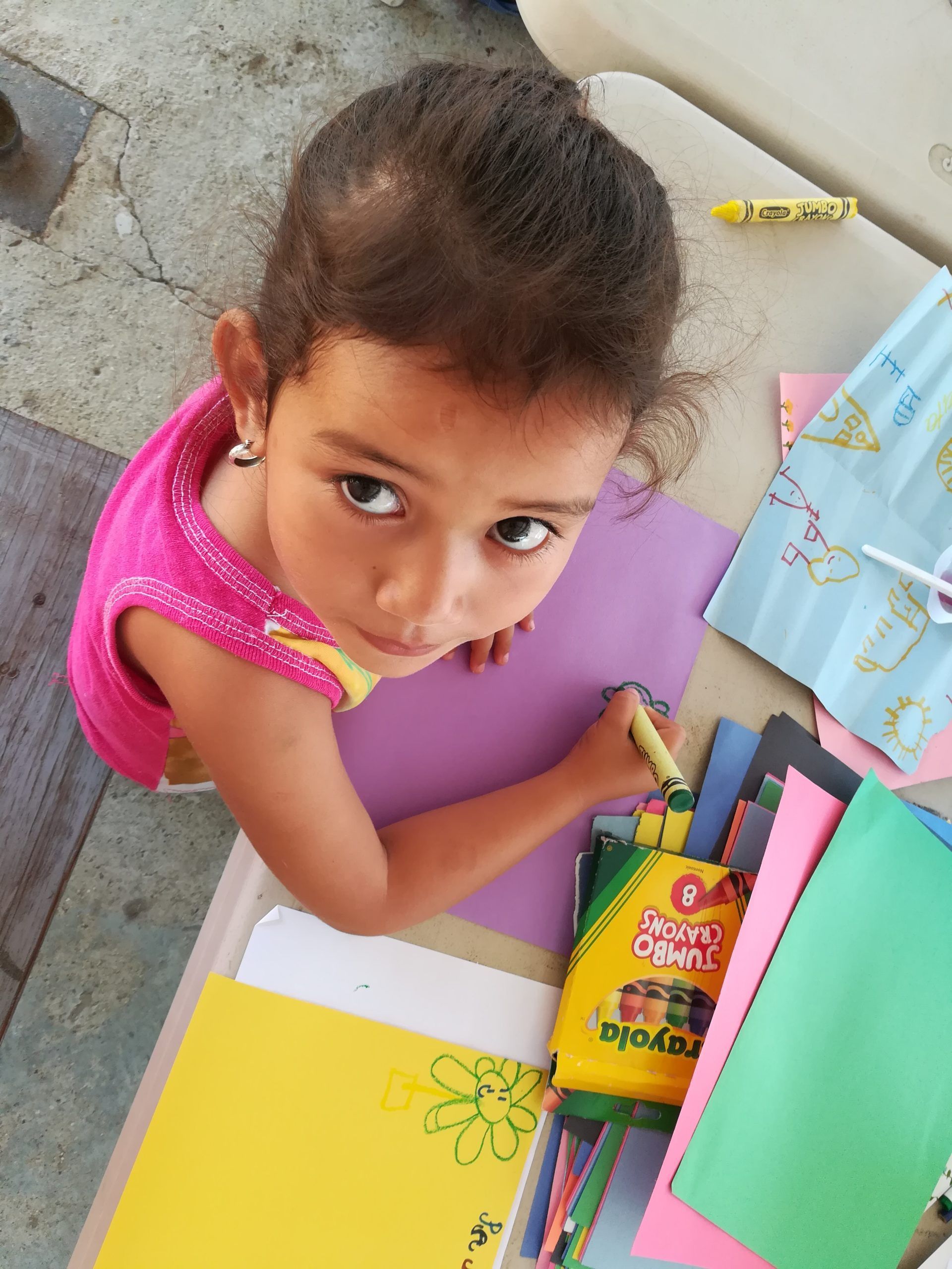 A little girl is sitting at a table drawing with crayola crayons