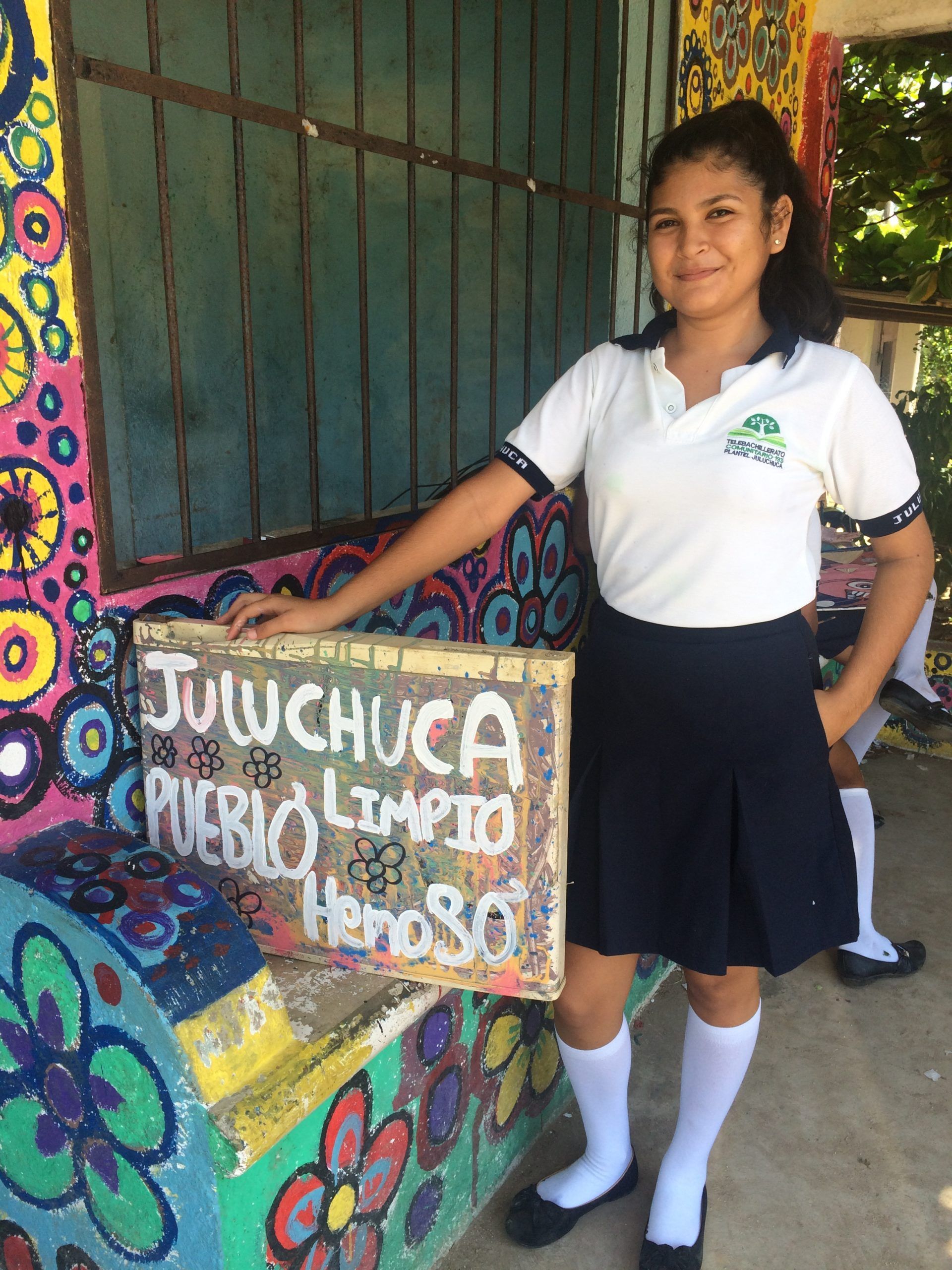A girl in a school uniform is holding a sign that says pueblo limpio