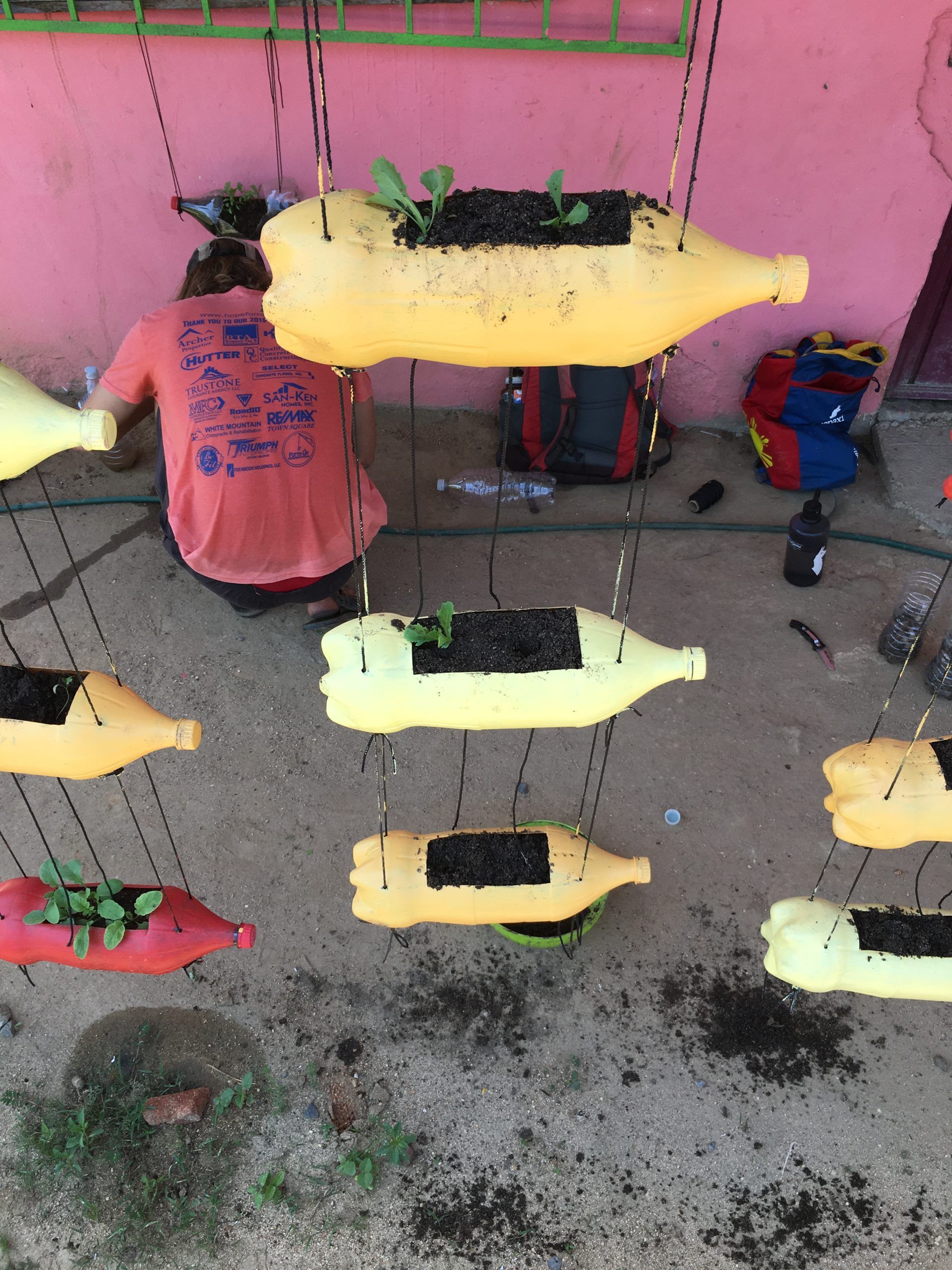 A person is sitting in front of a row of hanging planters made out of plastic bottles